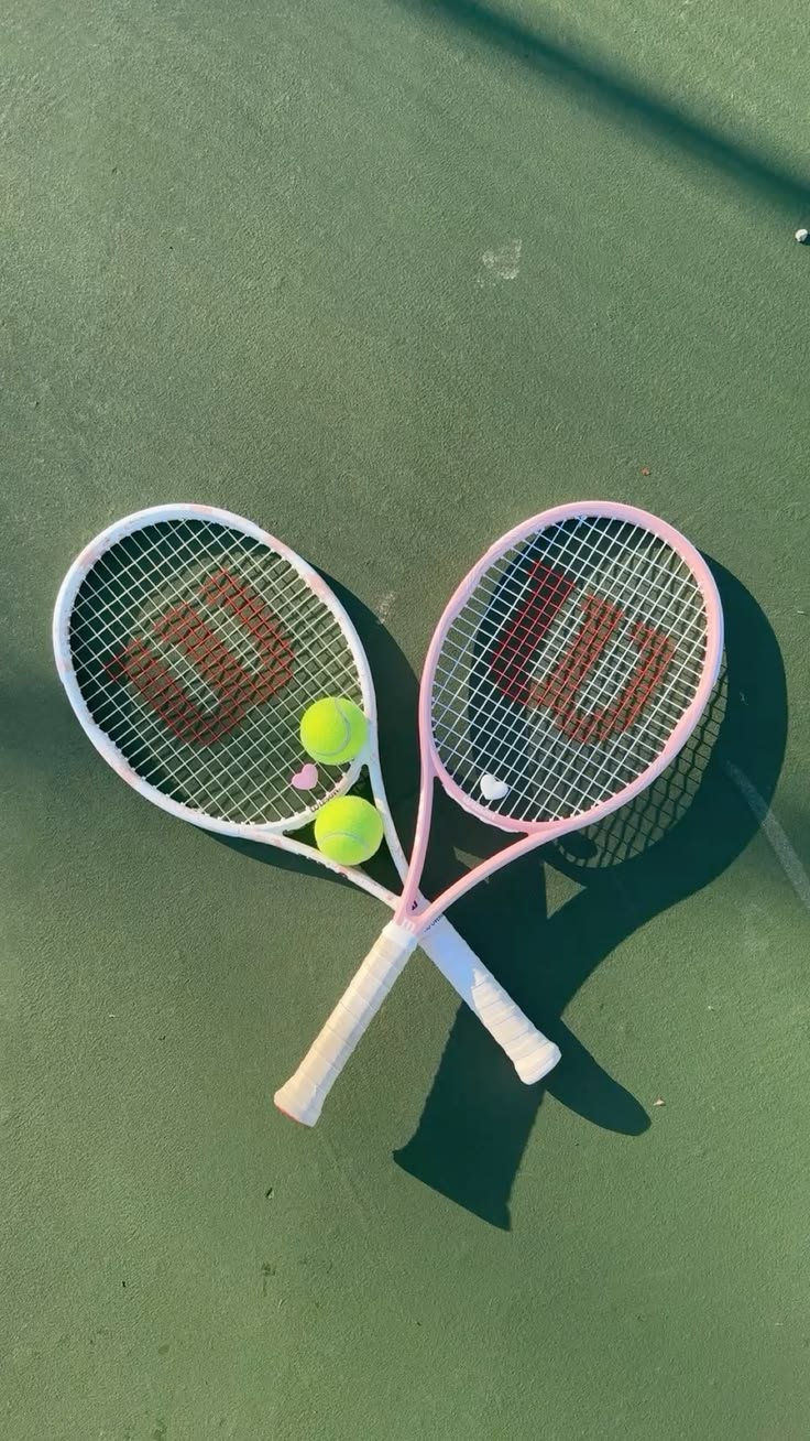 Pink and white tennis rackets crossed with optic yellow balls on a green hard court